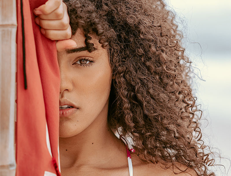 Frau mit lockigen braunen Haaren hält ein rotes Tuch vor ihr Gesicht.